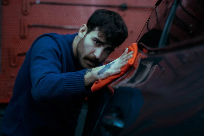 A person wiping a dark car panel with an orange cloth