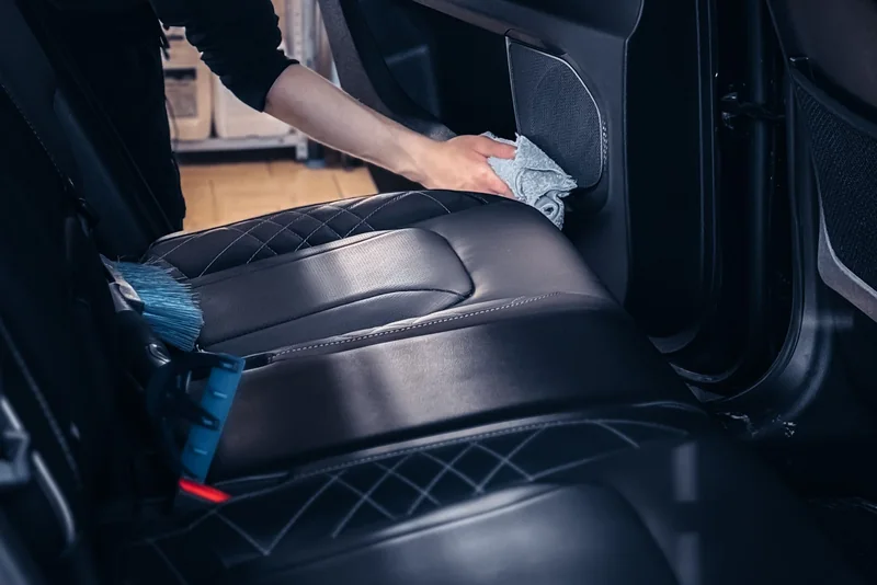 A person cleaning a black leather car seat with a cloth